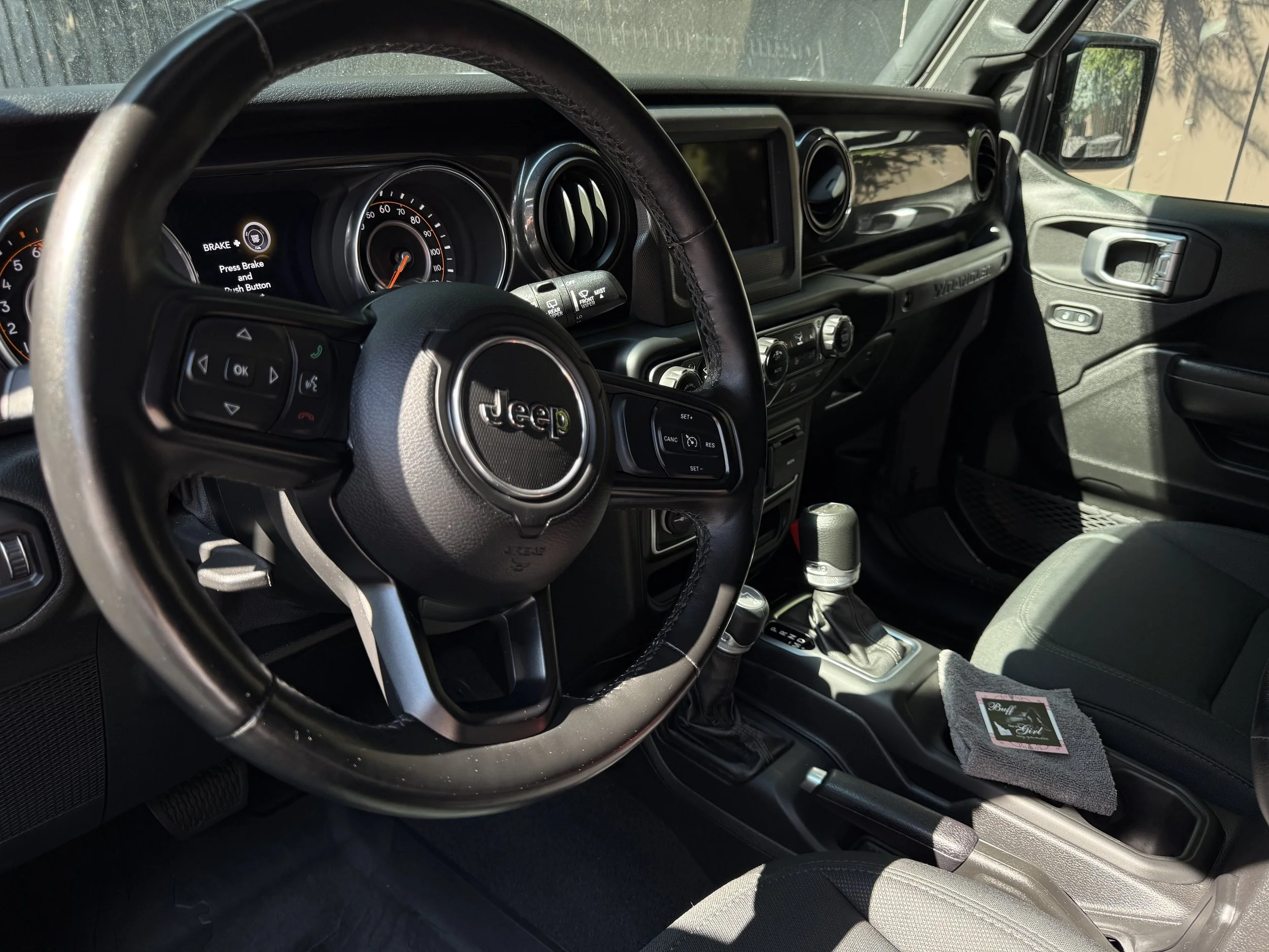 Interior view of the driver's cockpit showing steering wheel, dashboard, and modern Wrangler cabin