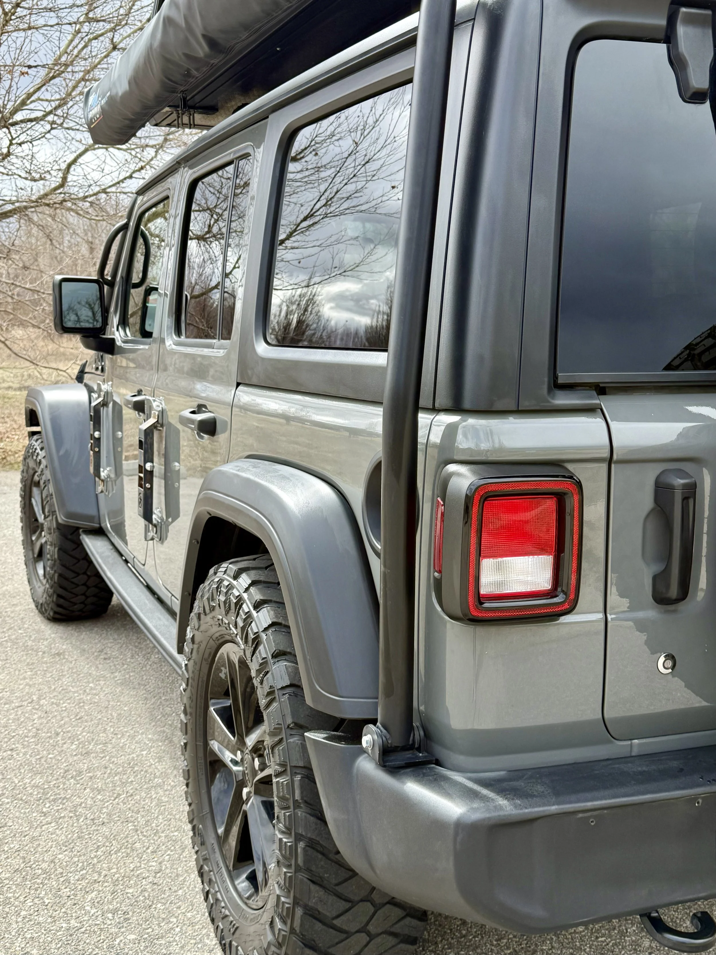 Detailed rear quarter view highlighting the exoskeleton, rugged tires, tail light, and roof-mounted overland gear