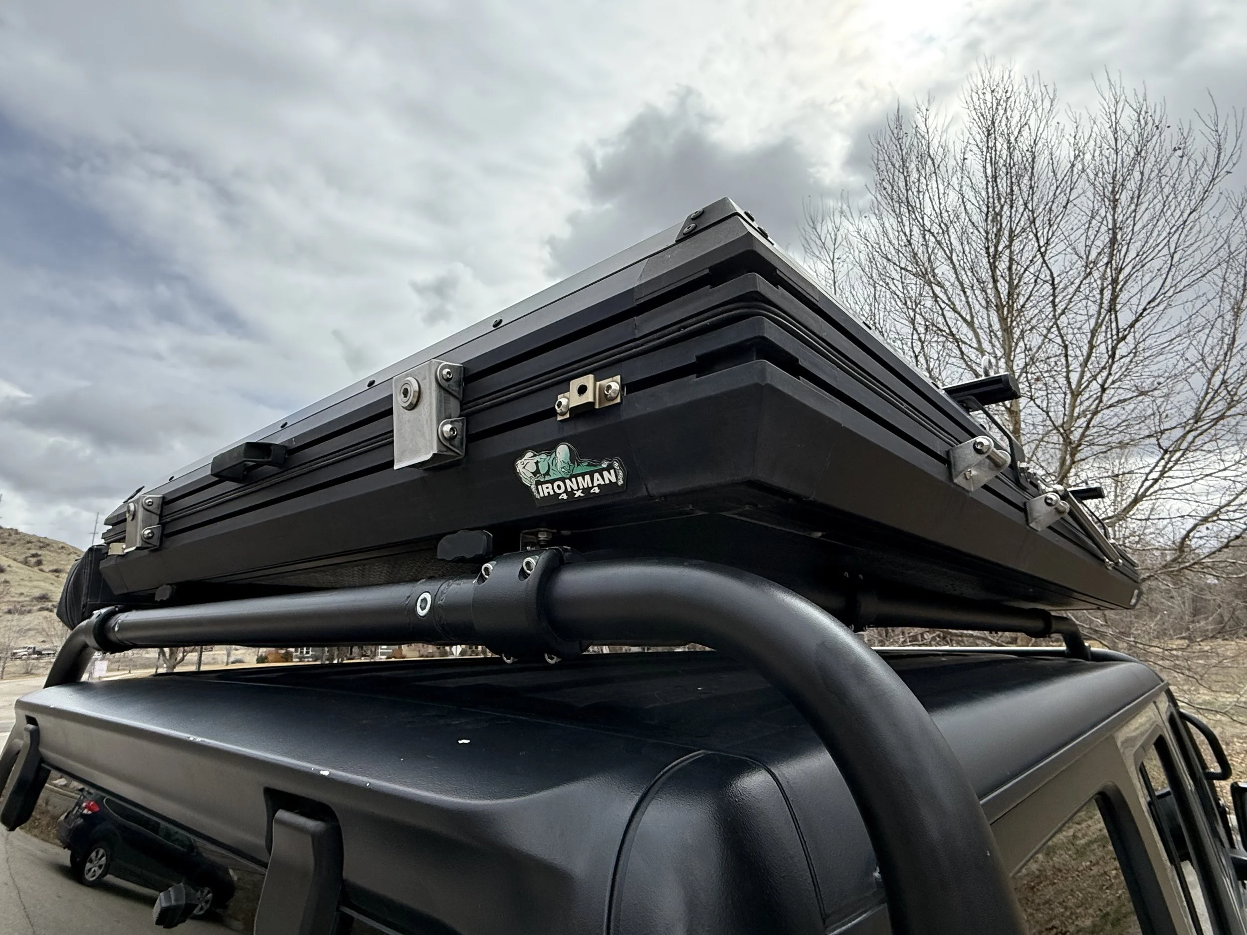 Low-angle close-up of the Ironman 4x4 hard-shell rooftop tent mounted on the roof rack, showing construction and latches