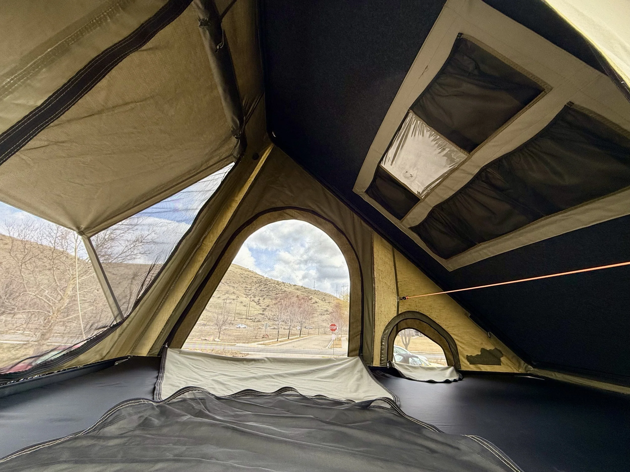 Interior view looking out from inside the hard-shell rooftop tent with landscape visible through the windows